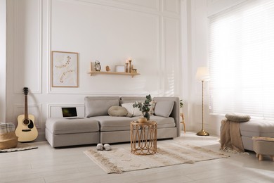 Living room with comfortable grey sofa, ottoman and stylish interior elements near window