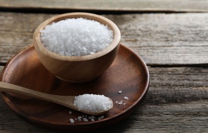 Photo of Organic salt in bowl and spoon on wooden table, closeup. Space for text