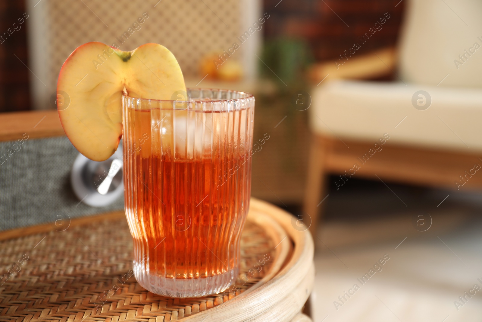 Photo of Relax at home. Glass of tasty cider on wicker table in room, closeup. Space for text