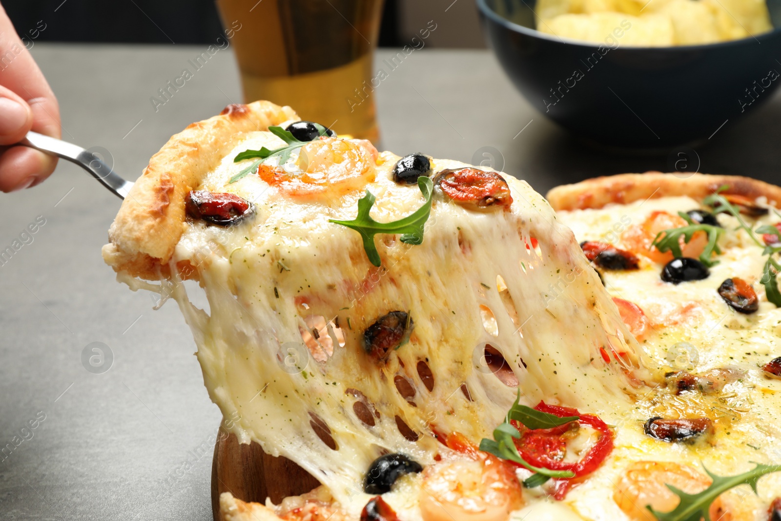 Photo of Woman taking slice of cheese pizza with seafood at table, closeup