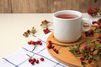 Photo of Cup with hawthorn tea and berries on beige table, space for text