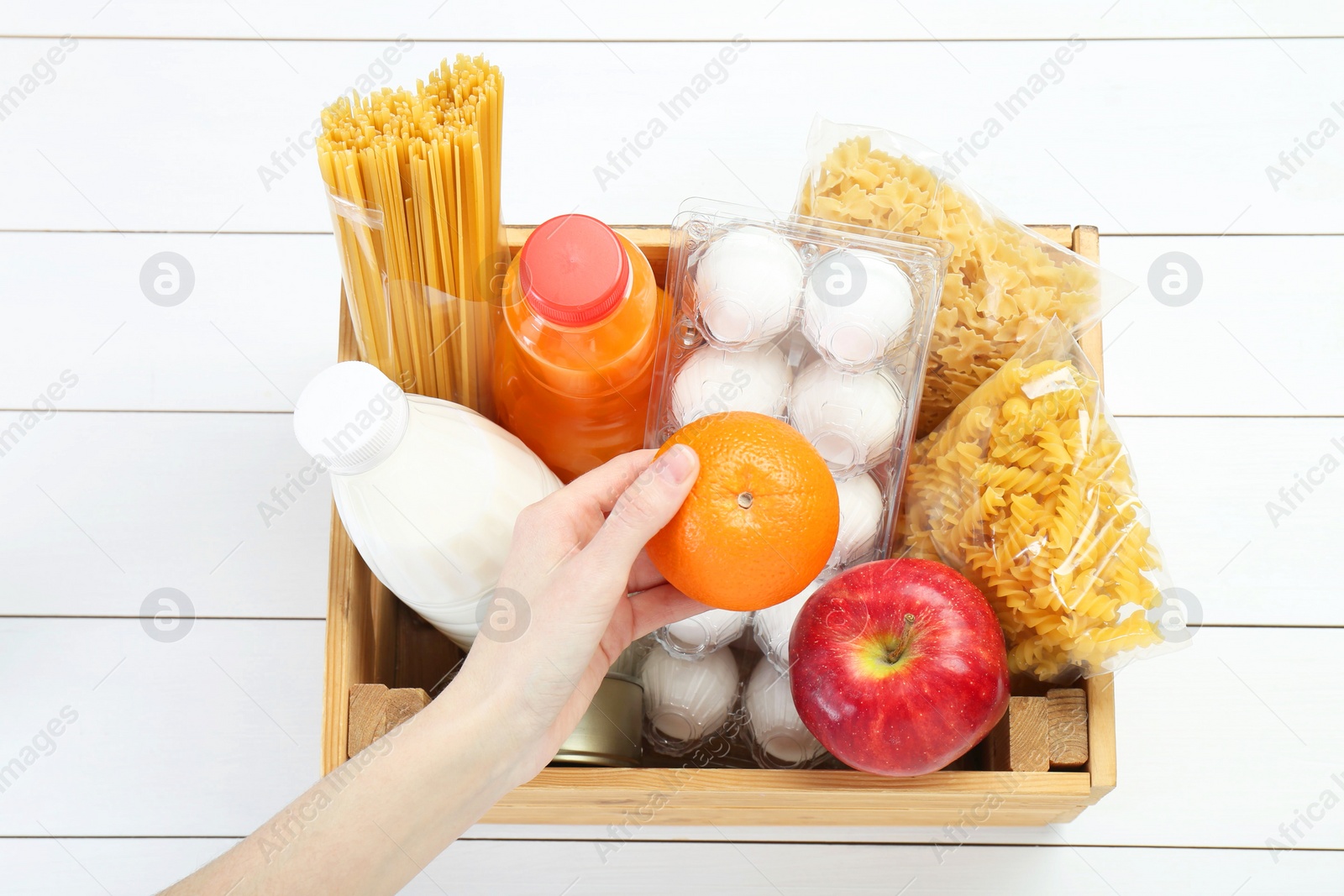 Photo of Humanitarian aid. Woman with food products for donation at white wooden table, top view