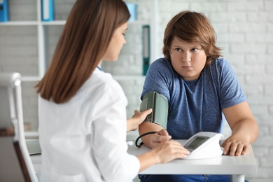 Female doctor checking overweight boy's blood pressure in clinic