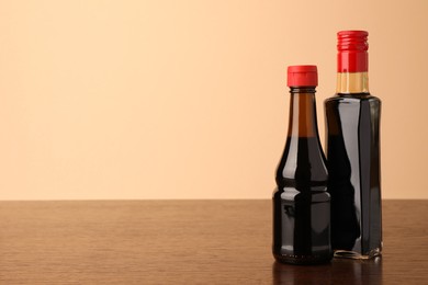 Photo of Bottles with soy sauce on wooden table against beige background. Space for text