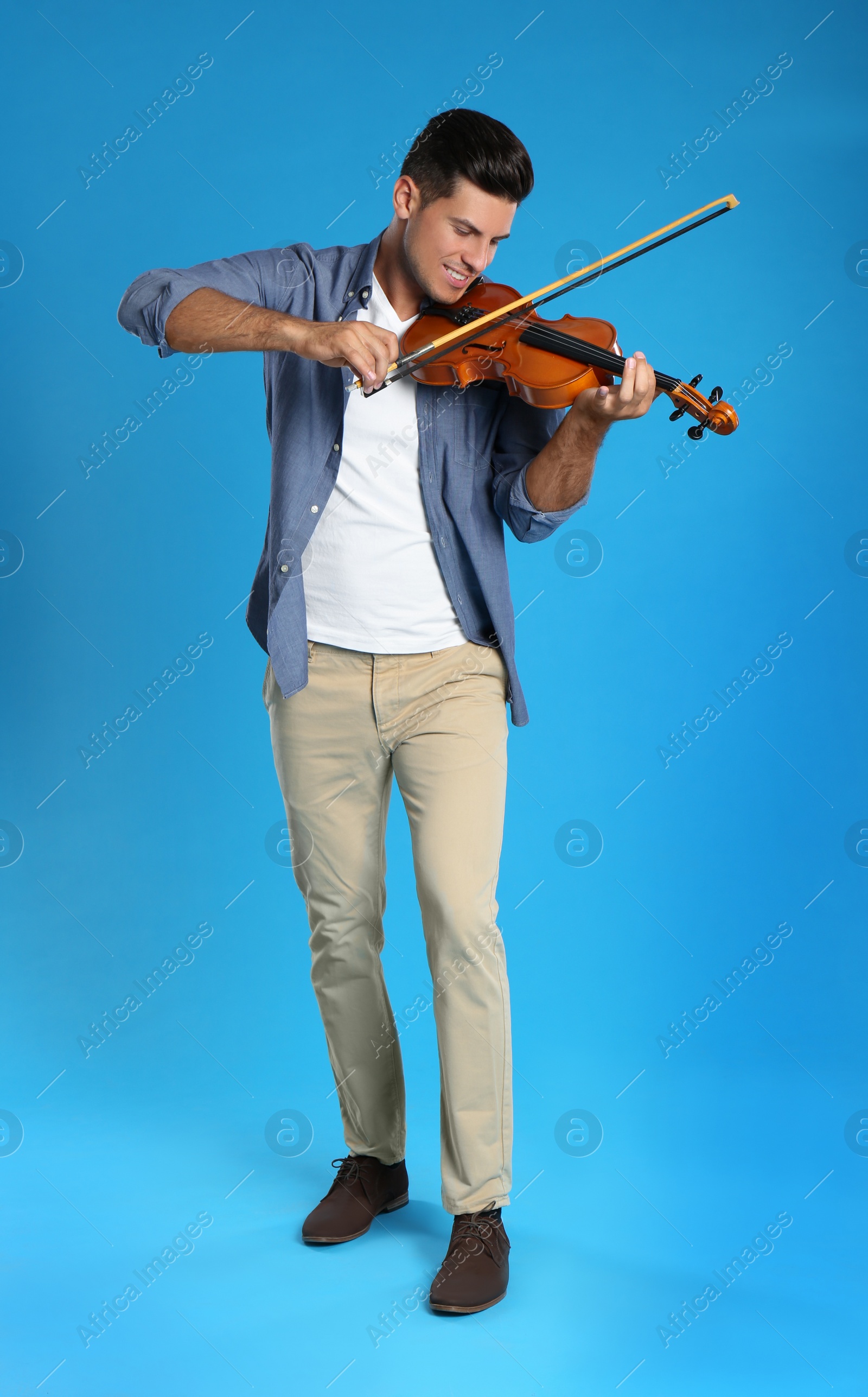 Photo of Happy man playing violin on light blue background