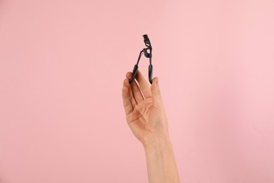Photo of Woman holding eyelash curler on pink background, closeup. Makeup tool