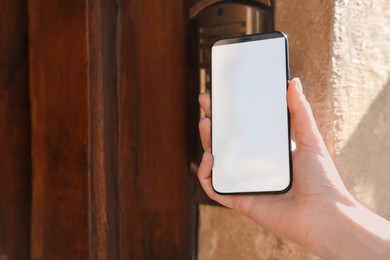 Woman opening door with smartphone outdoors, closeup
