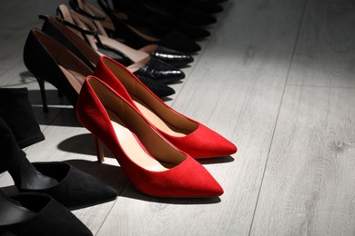 Photo of Red shoes among black ones on light wooden floor. Diversity concept
