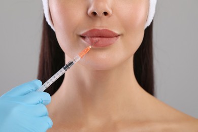 Photo of Doctor giving lips injection to young woman on light grey background, closeup. Cosmetic surgery