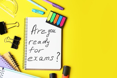 Photo of Notebook with phrase Are You Ready For Exams and stationery on yellow background, flat lay. Space for text