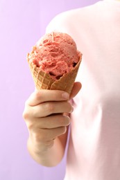 Photo of Woman holding pink ice cream in wafer cone on violet background, closeup