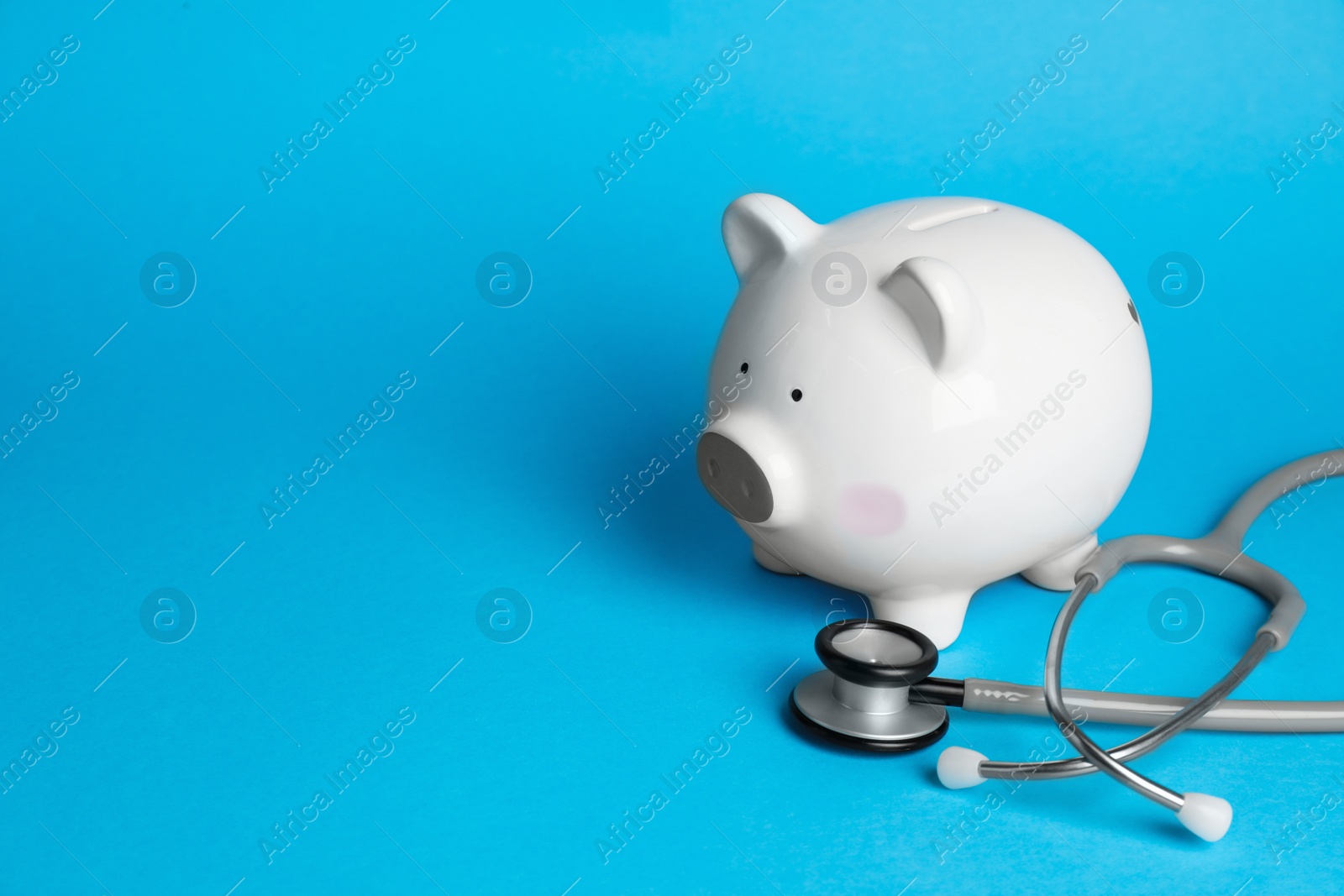 Photo of White ceramic piggy bank and stethoscope on light blue background, space for text. Medical insurance