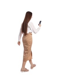 Photo of Young woman in casual outfit using smartphone while walking on white background