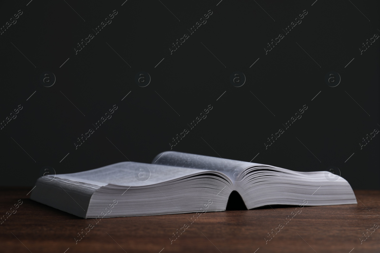 Photo of Open Bible on wooden table against black background, space for text. Religious book