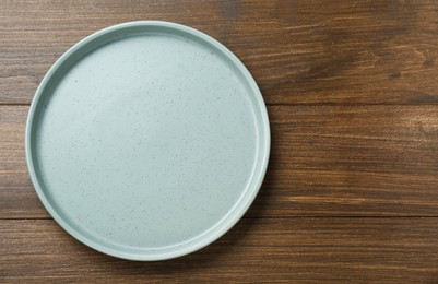 Photo of Empty ceramic plate on wooden table, top view. Space for text