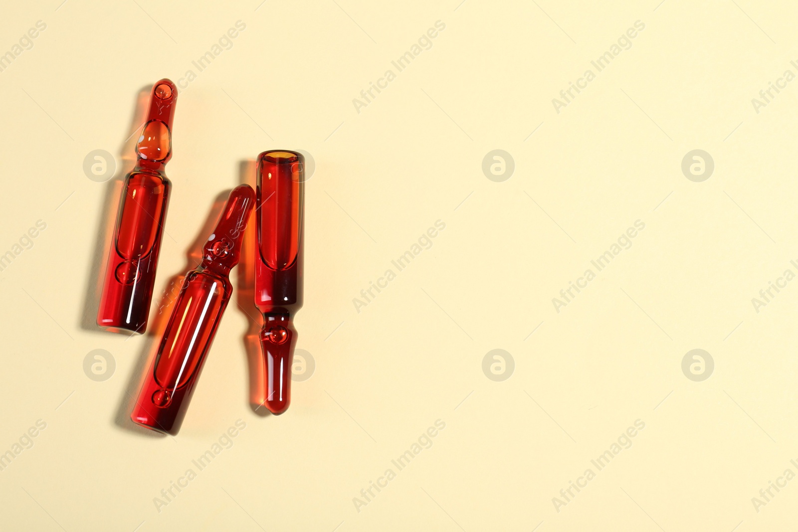 Photo of Glass ampoules with liquid on beige background, top view. Space for text