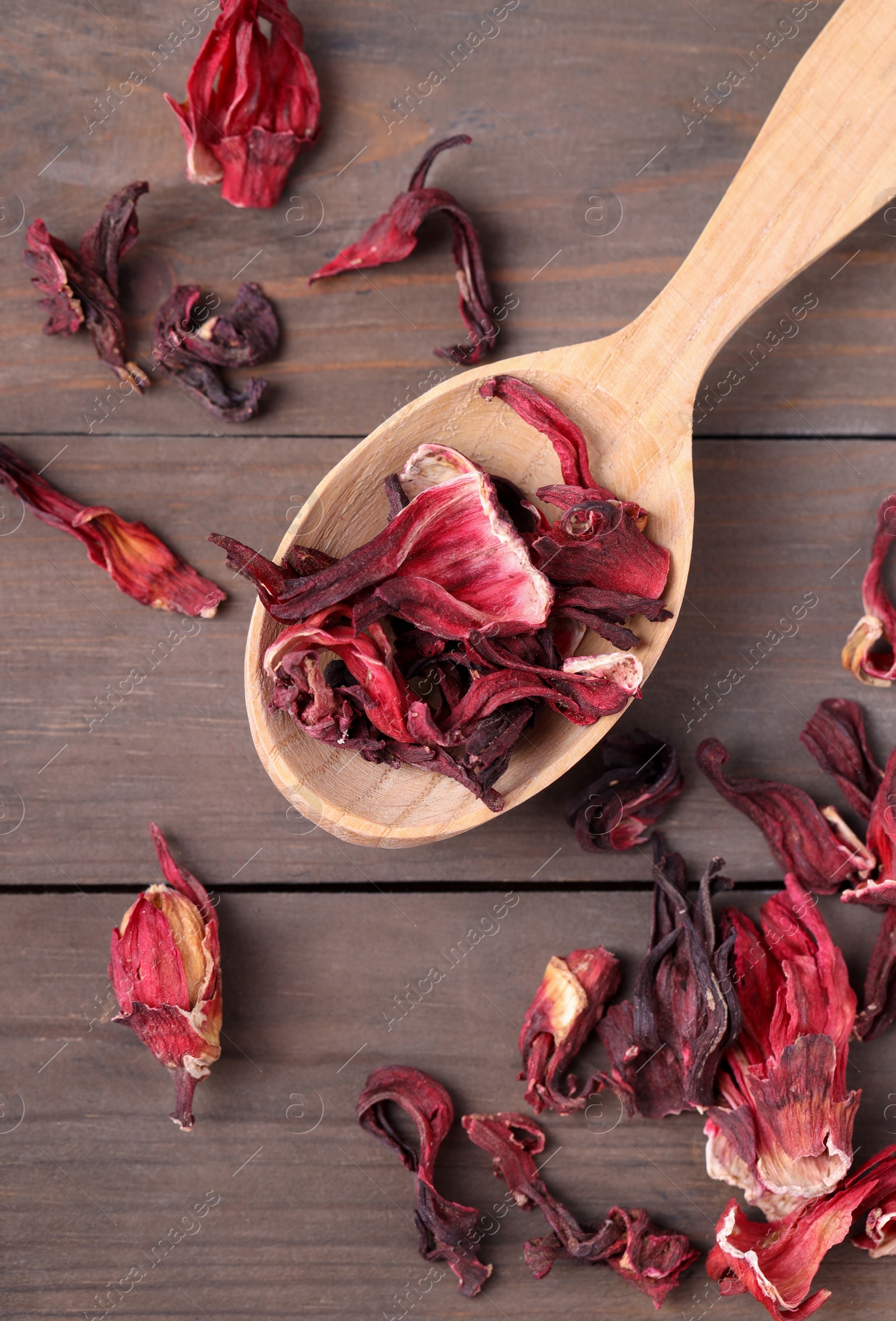 Photo of Spoon with dry hibiscus tea on wooden table, flat lay