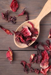 Photo of Spoon with dry hibiscus tea on wooden table, flat lay