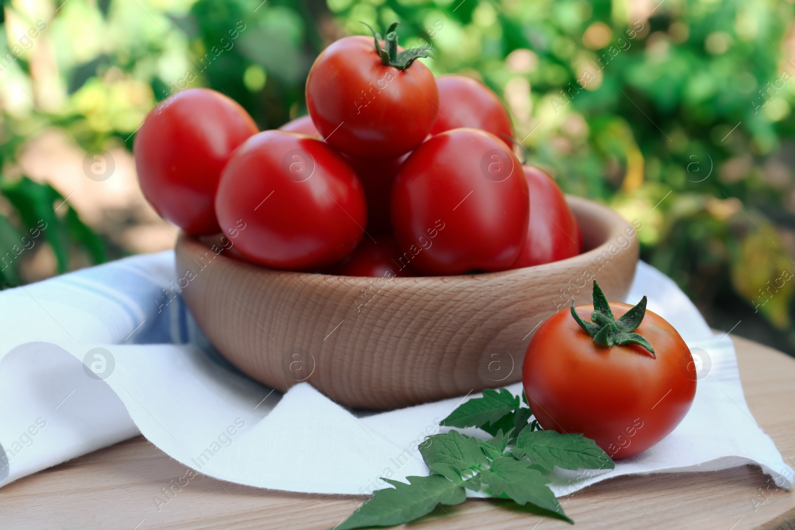 Photo of Bowl and fresh tomatoes on wooden table outdoors, closeup