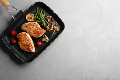 Frying pan with tasty grilled chicken fillets and vegetables on light grey table, top view. Space for text