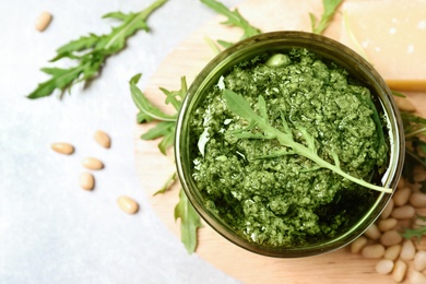 Bowl of tasty arugula pesto and ingredients on light table, flat lay