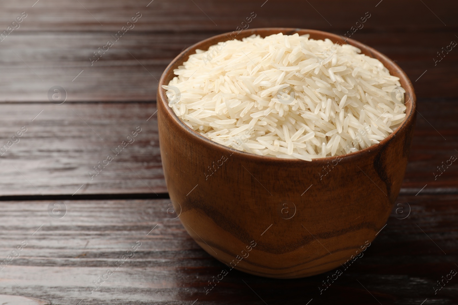 Photo of Raw basmati rice in bowl on wooden table, closeup. Space for text
