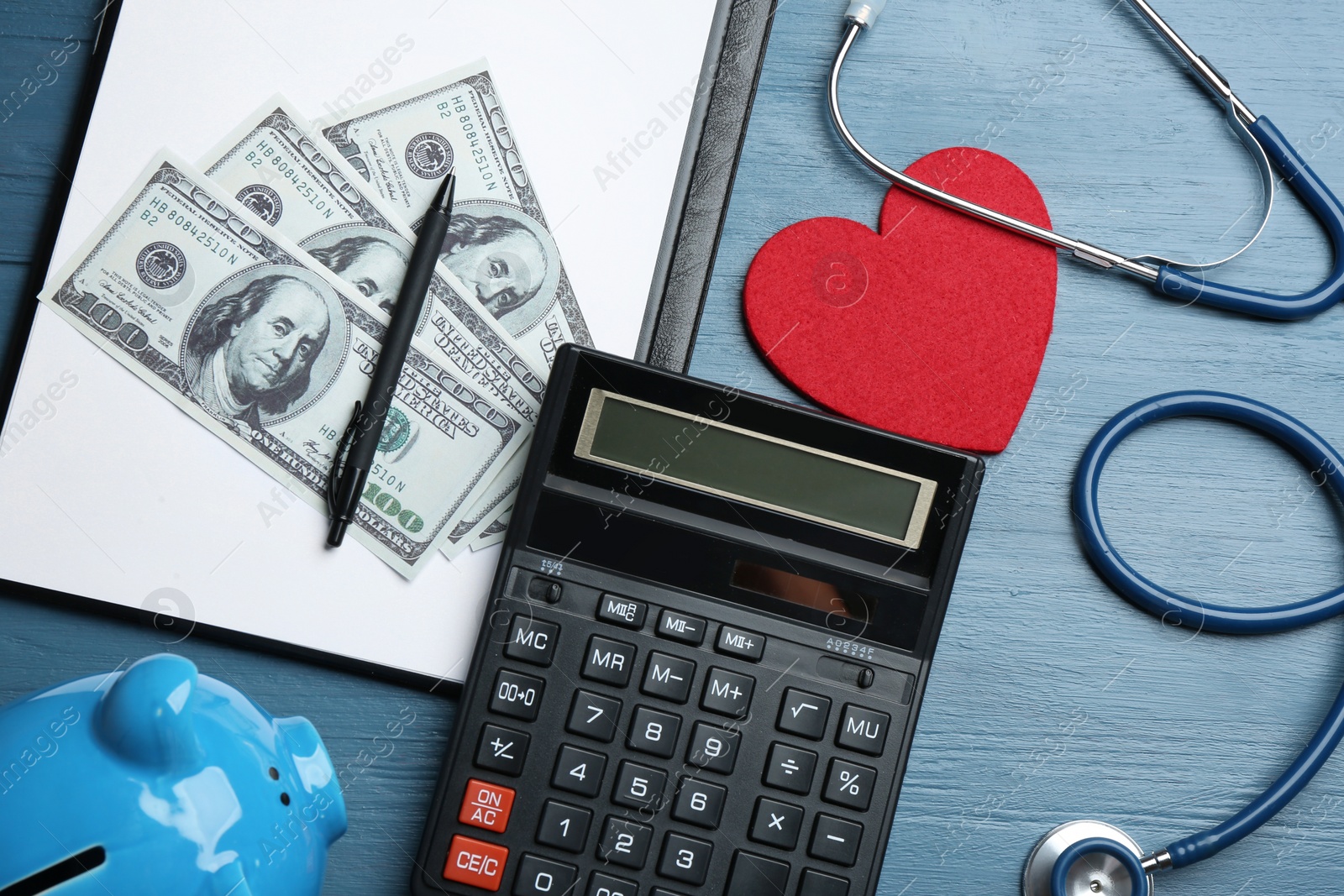 Photo of Flat lay composition with calculator, money and red heart on blue wooden surface. Health insurance concept