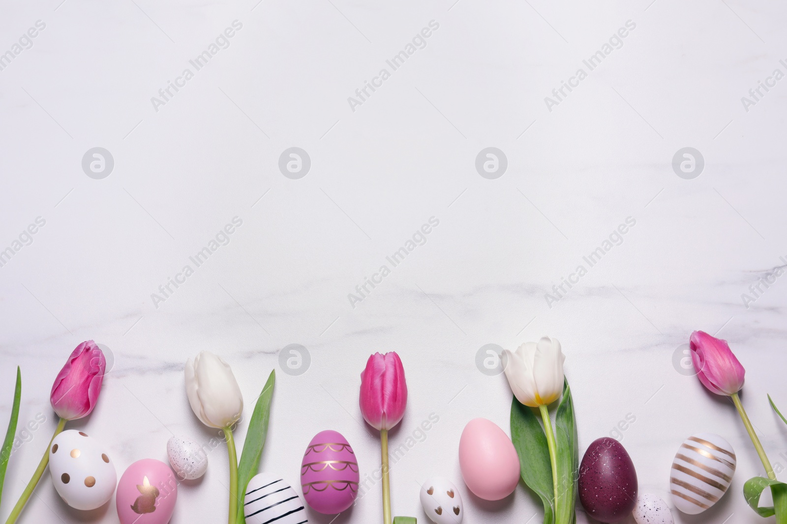 Photo of Flat lay composition of painted Easter eggs and tulip flowers on white marble table. Space for text