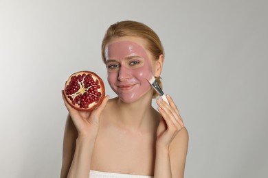 Photo of Young woman with pomegranate applying face mask on light grey background