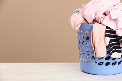 Photo of Plastic laundry basket with clothes near beige wall. Space for text