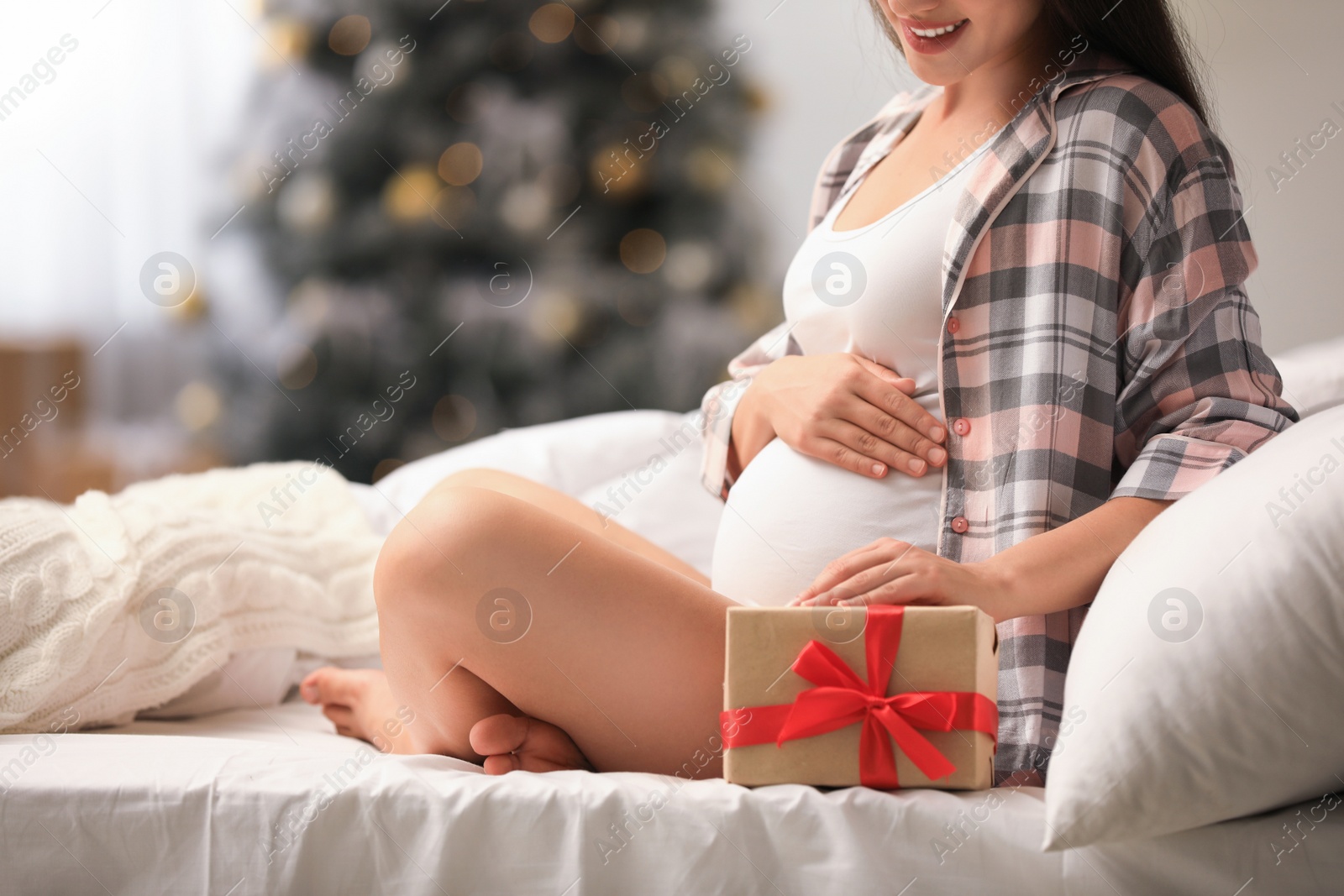 Photo of Happy pregnant woman with Christmas gift box on bed at home, closeup. Expecting baby