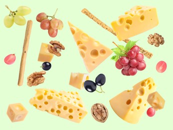 Cheese, breadsticks, grapes and walnuts falling against pale light green background