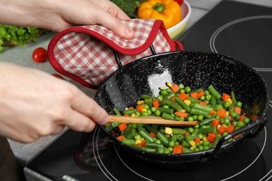 Photo of Woman cooking tasty vegetable mix in wok pan at home, closeup