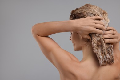 Photo of Woman washing hair on light grey background, back view. Space for text