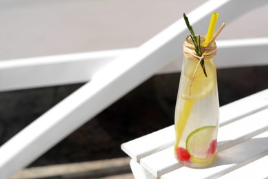 Photo of Refreshing tasty lemonade served in glass bottle on white deck chair. Space for text
