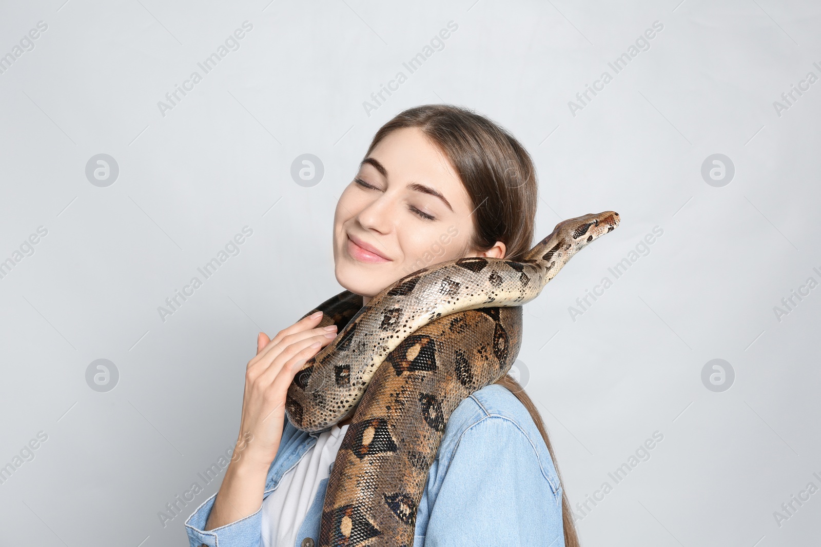 Photo of Young woman with boa constrictor on light background. Exotic pet