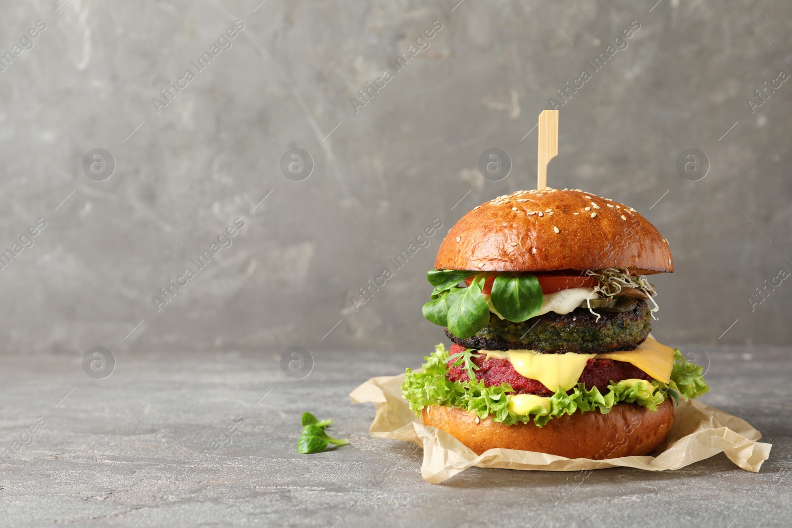 Photo of Vegan burger with beet and falafel patties on table against grey background. Space for text