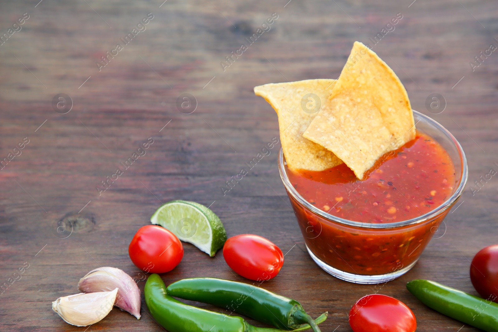 Photo of Tasty salsa sauce with tortilla chips and ingredients on wooden table, space for text