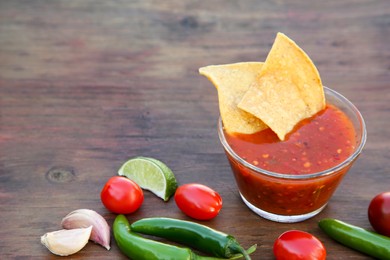 Tasty salsa sauce with tortilla chips and ingredients on wooden table, space for text