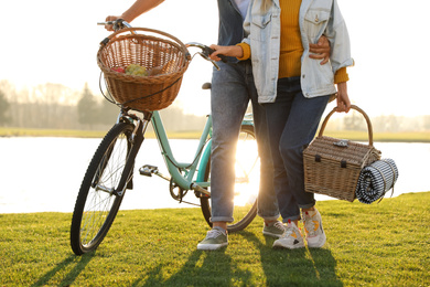 Young couple with bicycle and picnic basket near lake on sunny day, closeup