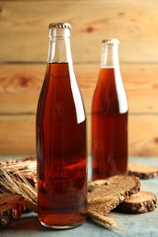 Photo of Bottles of delicious fresh kvass, spikelets and bread on blue wooden table