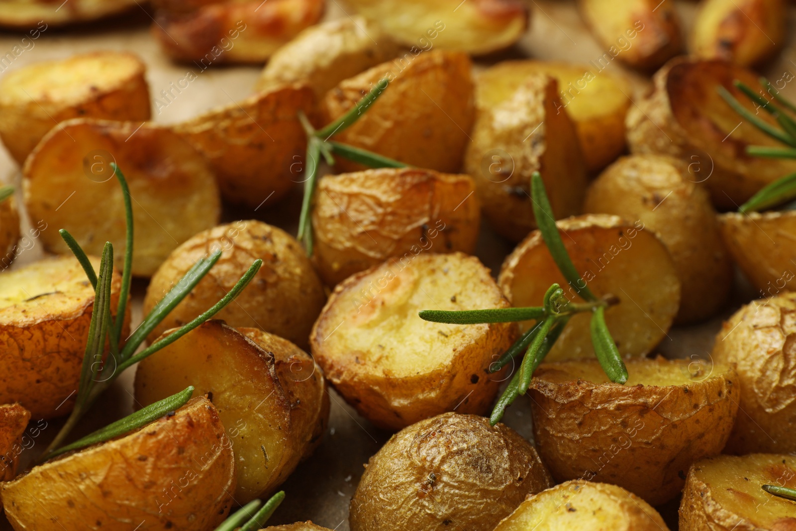 Photo of Tasty baked potato and aromatic rosemary on parchment paper, closeup