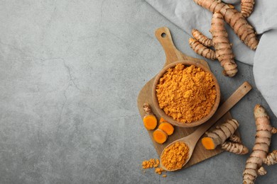Photo of Aromatic turmeric powder and raw roots on grey table, flat lay. Space for text