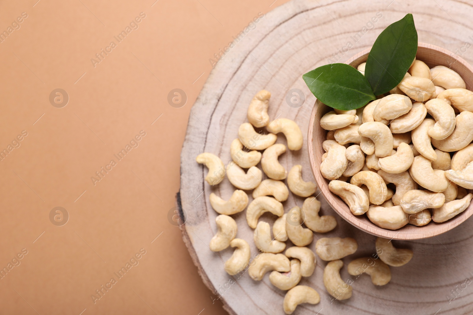 Photo of Tasty cashew nuts and green leaves on pale brown background, top view. Space for text