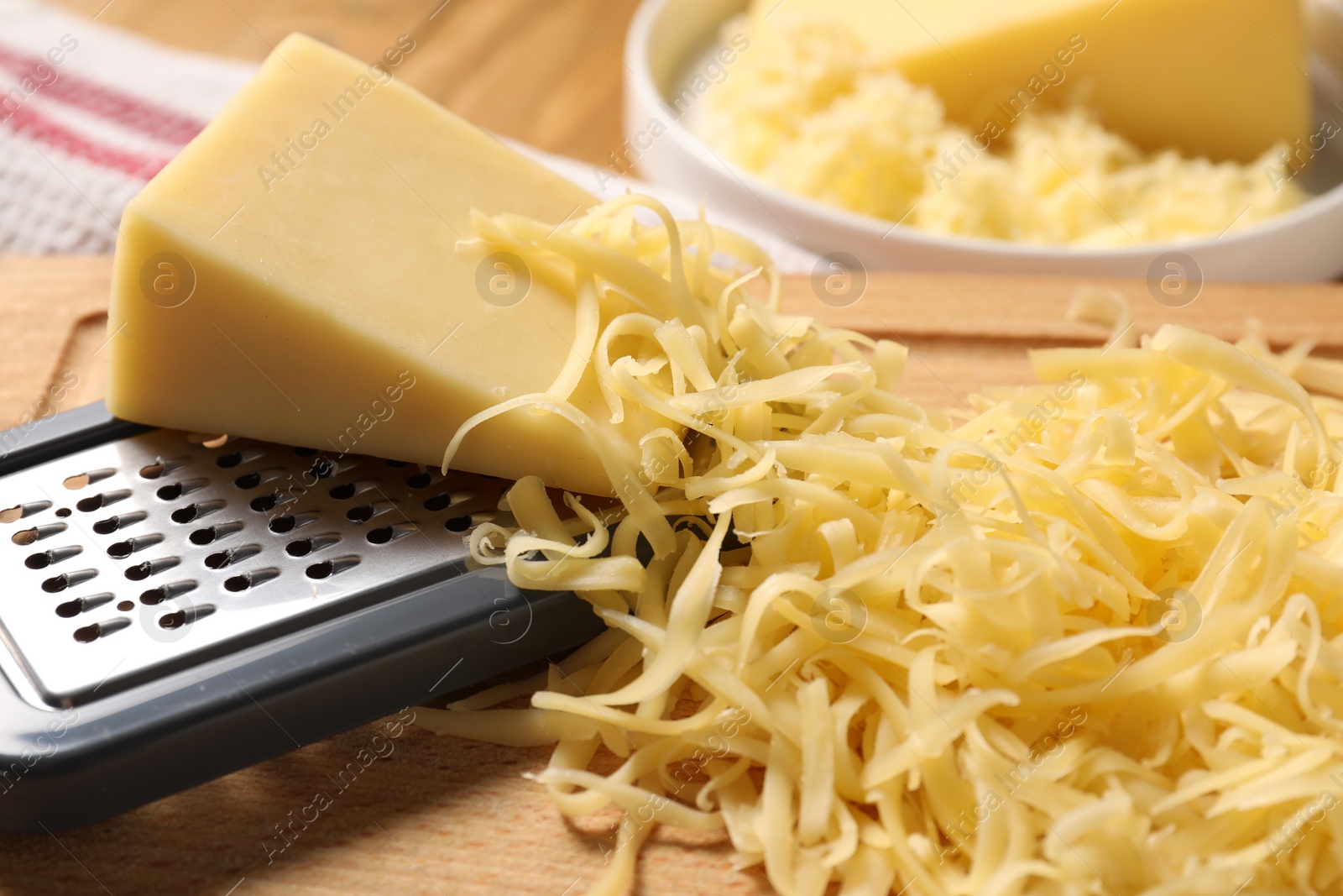 Photo of Grated, whole piece of cheese and grater on table, closeup