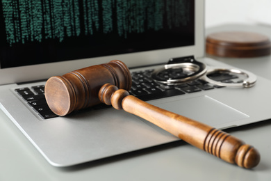 Photo of Laptop, wooden gavel and handcuffs on light table, closeup. Cyber crime