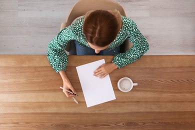 Woman writing on sheet of paper at table indoors, top view