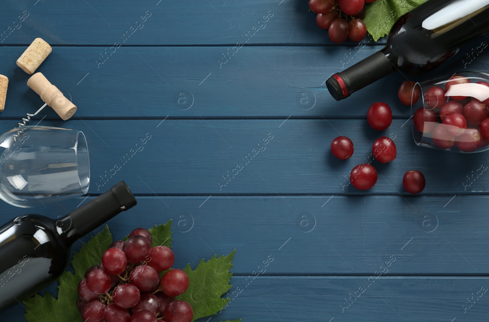 Photo of Bottles of red wine, glasses and grapes on blue wooden table, flat lay. Space for text