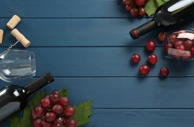 Photo of Bottles of red wine, glasses and grapes on blue wooden table, flat lay. Space for text