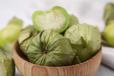 Fresh green tomatillos with husk in bowl on table, closeup
